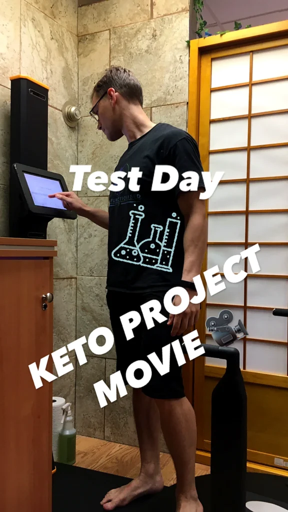 A person in a black t-shirt with a science-themed graphic stands next to a touchscreen kiosk, labeled 'Test Day.'