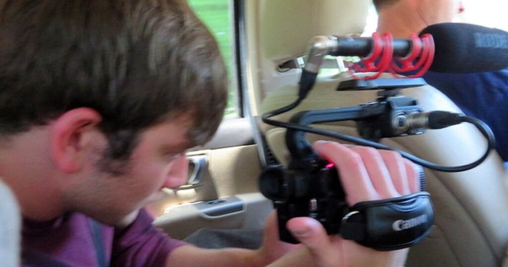 A young man focuses on filming with a camera inside a vehicle.