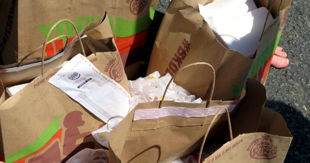 A pile of fast food bags and receipts from Burger King on the ground.