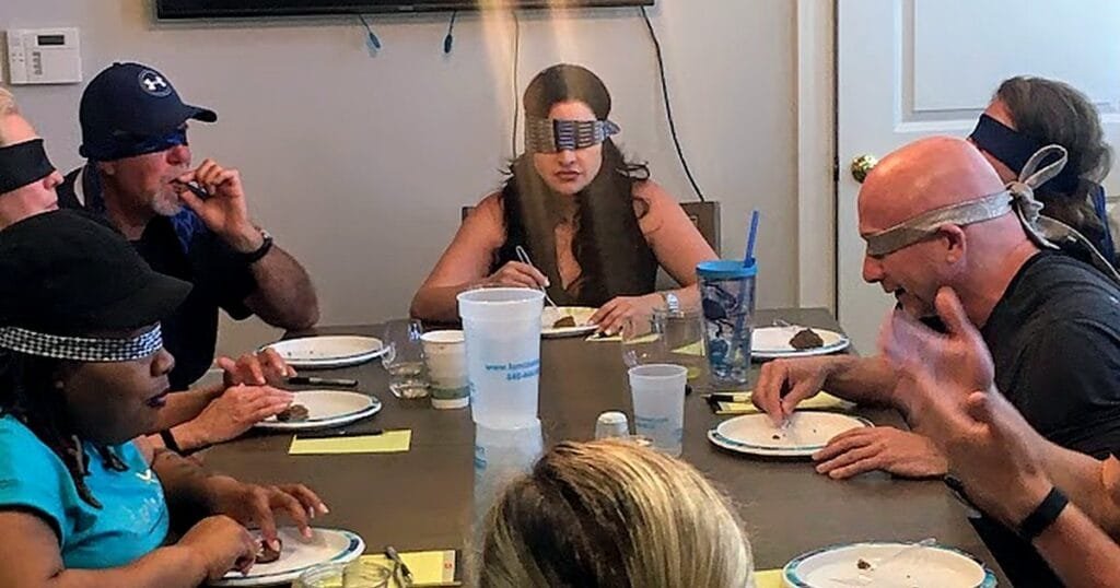 A group of people at a table, blindfolded, tasting food. Some are writing notes while others are eating.