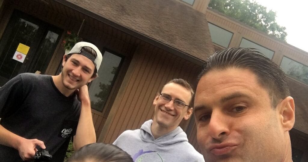 A group of four people posing for a selfie outside a building on a cloudy day.