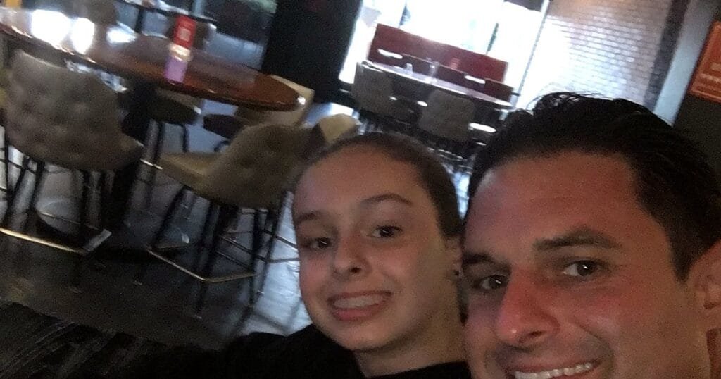 A man and a girl take a selfie in a restaurant with empty tables in the background.