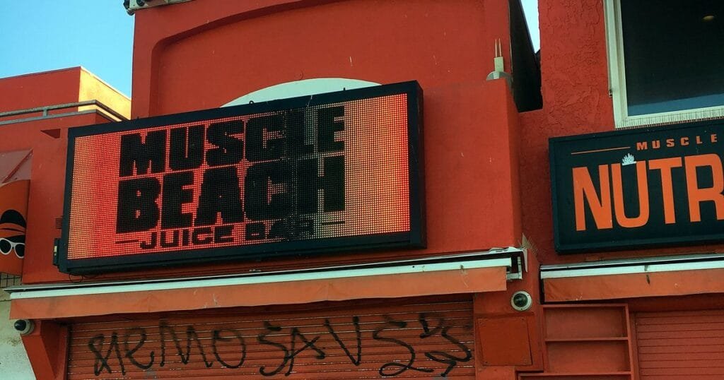 A bright LED sign reading 'MUSCLE BEACH JUICE CO.' on a red building.